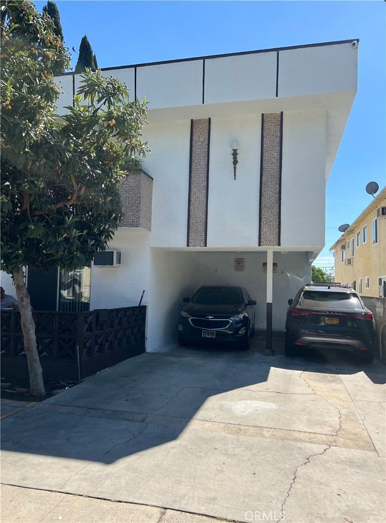 Front elevation of 14218 Sylvan Street showing the carport entry, mid-century stone-aggregate accent panels, period sconce lighting, and bracketed eaves above the second story