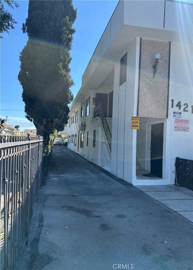 Side access alley running the length of 14218 Sylvan with second-story tenant balconies, exterior staircase to the upper units, and a tall Italian cypress flanking the property